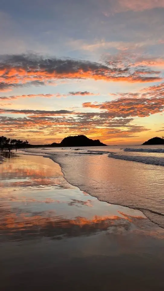 leuchtender Sonnenuntergang über einem Strand mit Spiegelungen im nassen Sand