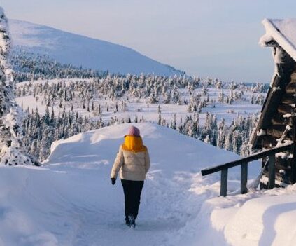 A woman walking through deep snow with snow-covered mountains in the background.